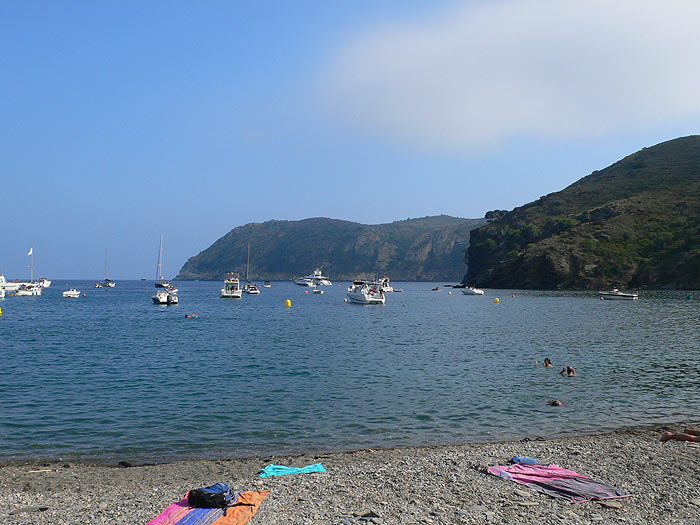Playa de piedras de la Cala Jòncols con el Cap de Norfeu al fondo 