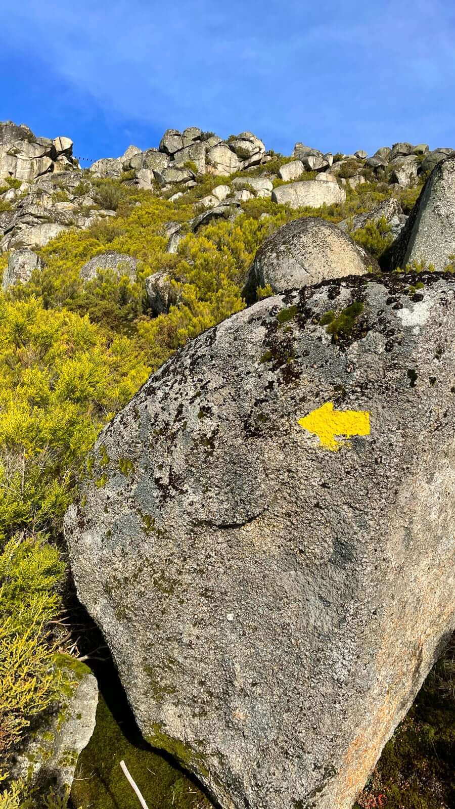 Flecha amarilla del camino de aproximación con la pasarela de la vía ferrata al fondo 