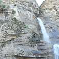 La cascada baja con fuerza en época de deshielo. Al costado se puede ver gente accediendo a la cueva 